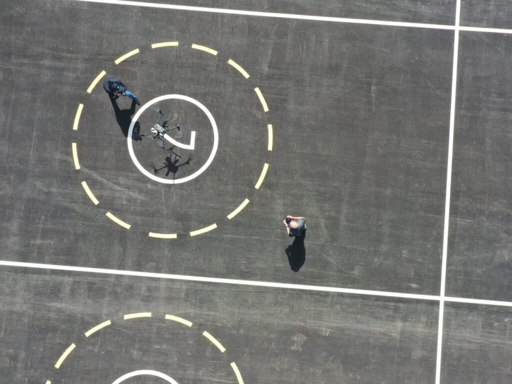 Aerial view of a drone testing port at Future Mobility Campus Ireland (FMCI), showing a large, marked landing pad with two drone operators. The facility supports research and development in urban air mobility, autonomous flight systems, and unmanned aerial vehicle (UAV) integration