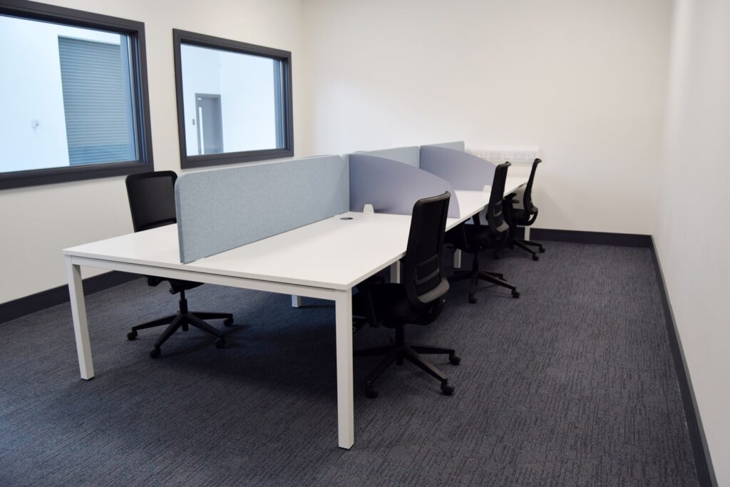 A private research and development office space with white desks and black ergonomic chairs, divided by light blue privacy panels. The layout is ideal for startups, remote workers, and businesses looking for flexible office rentals.